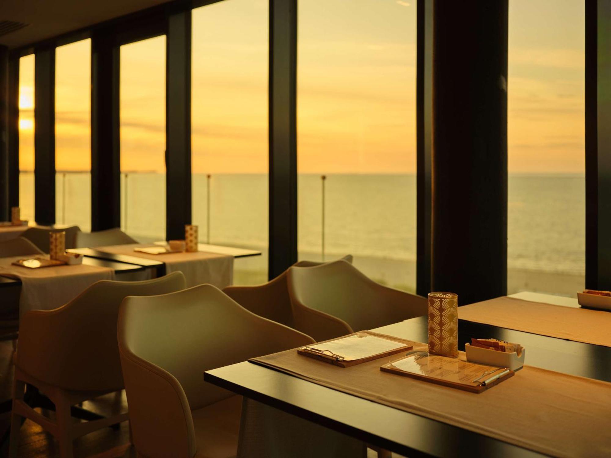 Radisson Blu Resort シフィノウイシチェ エクステリア 写真 The photo shows a restaurant interior with a beautiful view of the ocean during sunset. The large windows allow natural light to flood the space, highlighting the warm colors of the sunset in the sky. There are several tables, each set with placemats