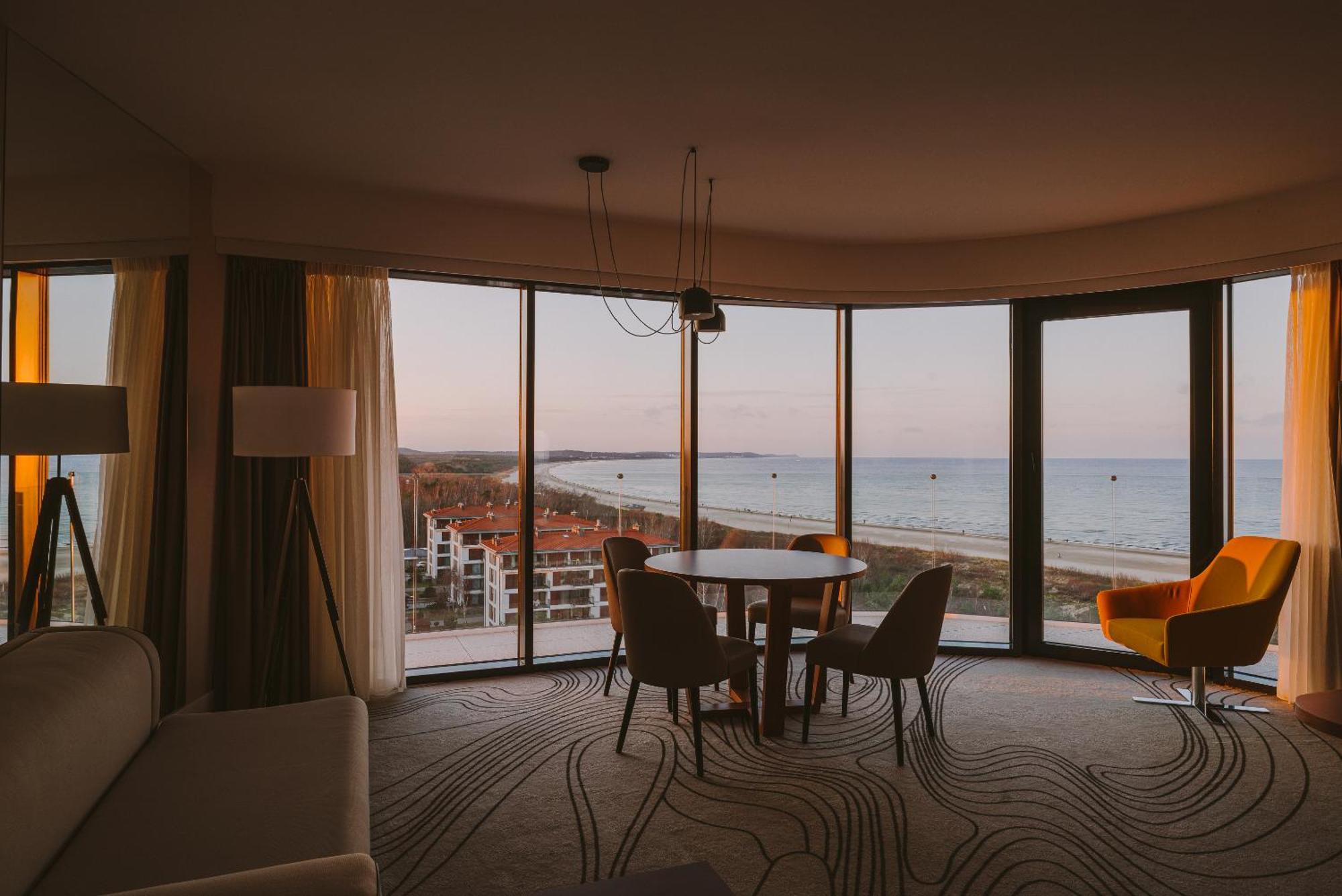 Radisson Blu Resort シフィノウイシチェ エクステリア 写真 The photo shows a modern and stylish interior of a room featuring large windows that provide a view of the beach and ocean. The room is furnished with a round table and chairs, along with a cozy sofa and a bright yellow armchair. The decor has a cont