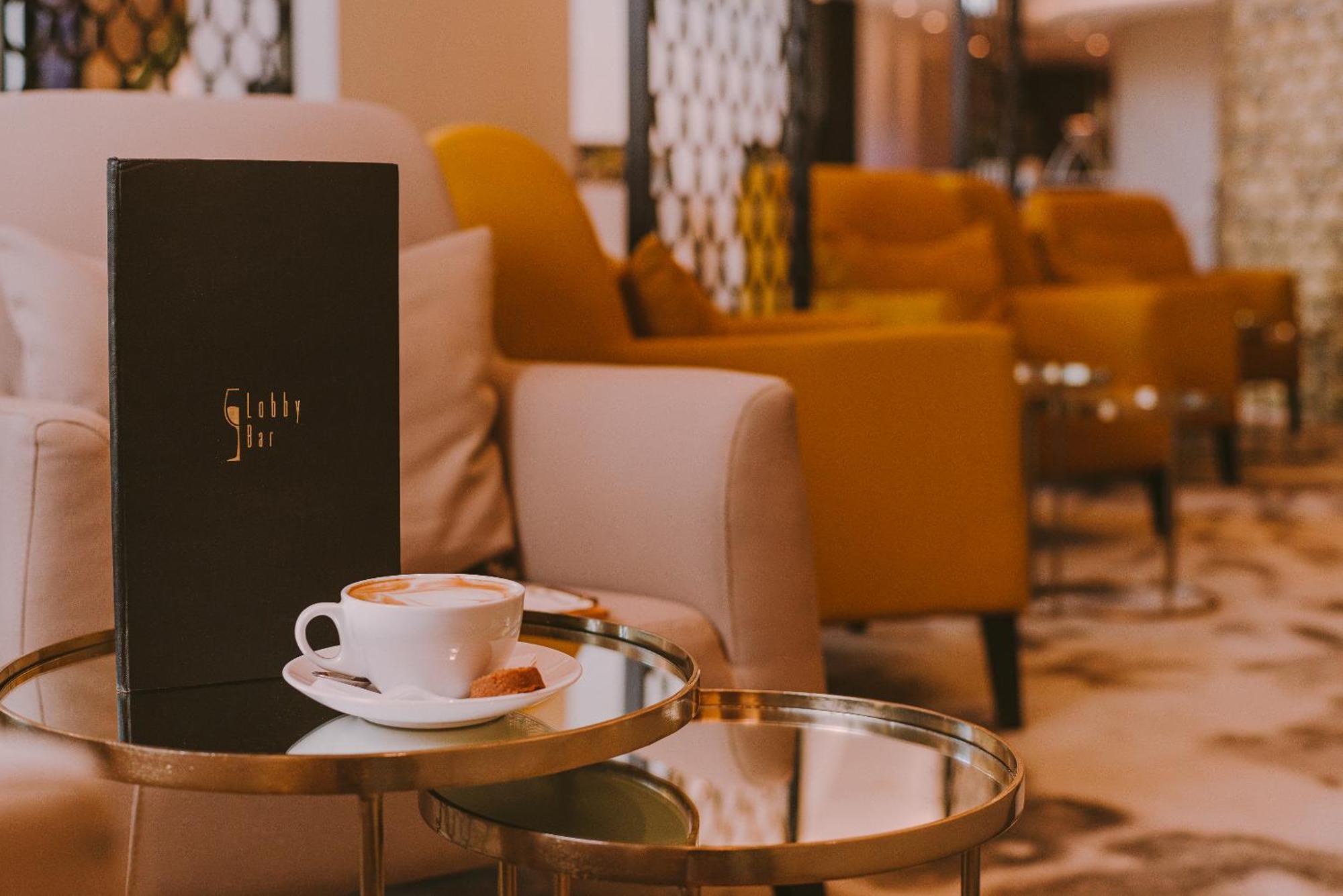 Radisson Blu Resort シフィノウイシチェ エクステリア 写真 The photo shows a cozy indoor setting with a stylish, modern atmosphere. In the foreground, there is a small round glass table with a white coffee cup and a saucer, alongside a small biscuit or cookie. Next to the coffee, there is a black menu with e