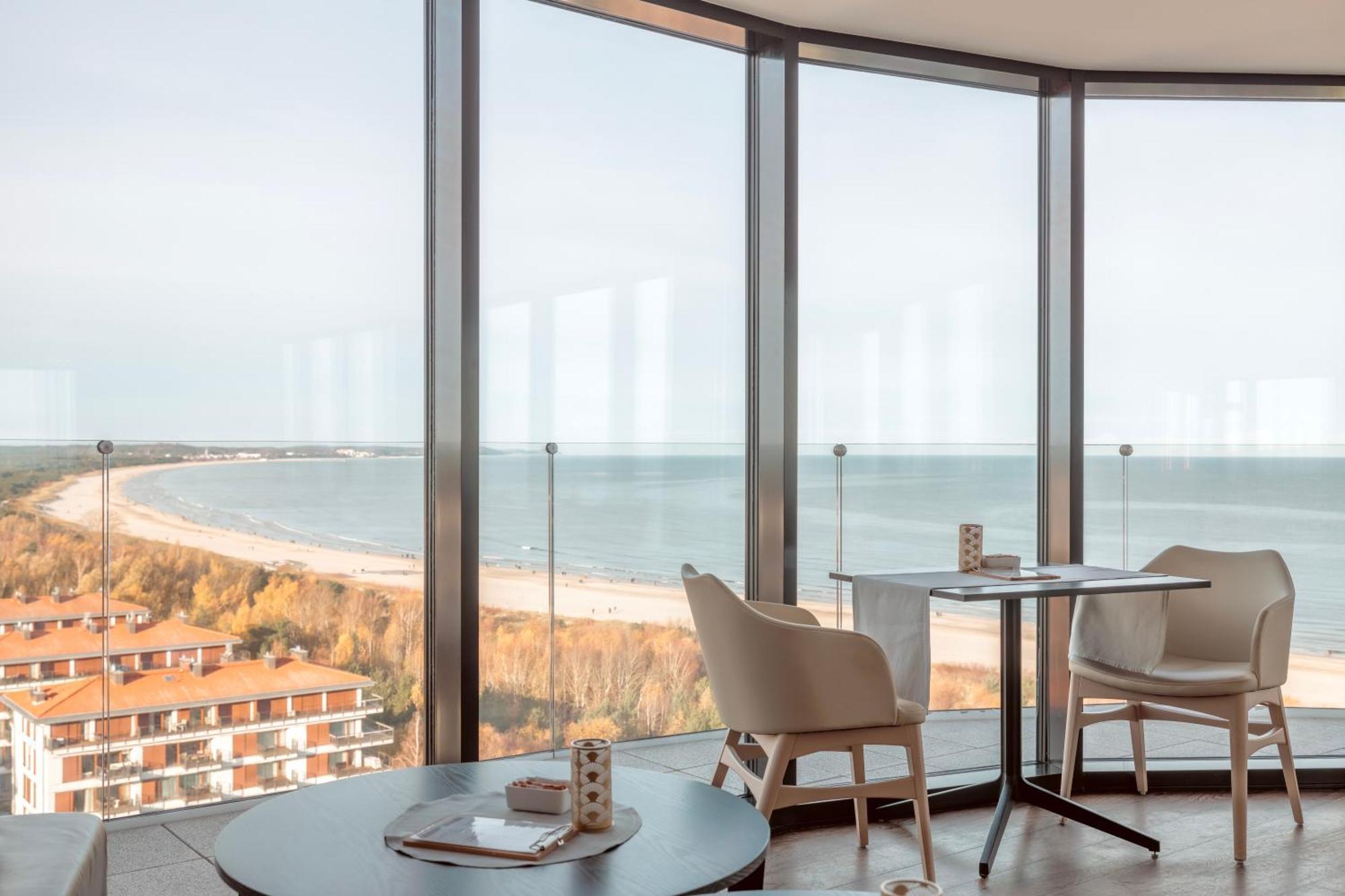 Radisson Blu Resort シフィノウイシチェ エクステリア 写真 The photo shows a modern interior space with large floor-to-ceiling windows that provide a stunning view of the beach and sea. The area appears to be a dining or lounge space, featuring a minimalistic table and chairs. There is a sense of tranquility