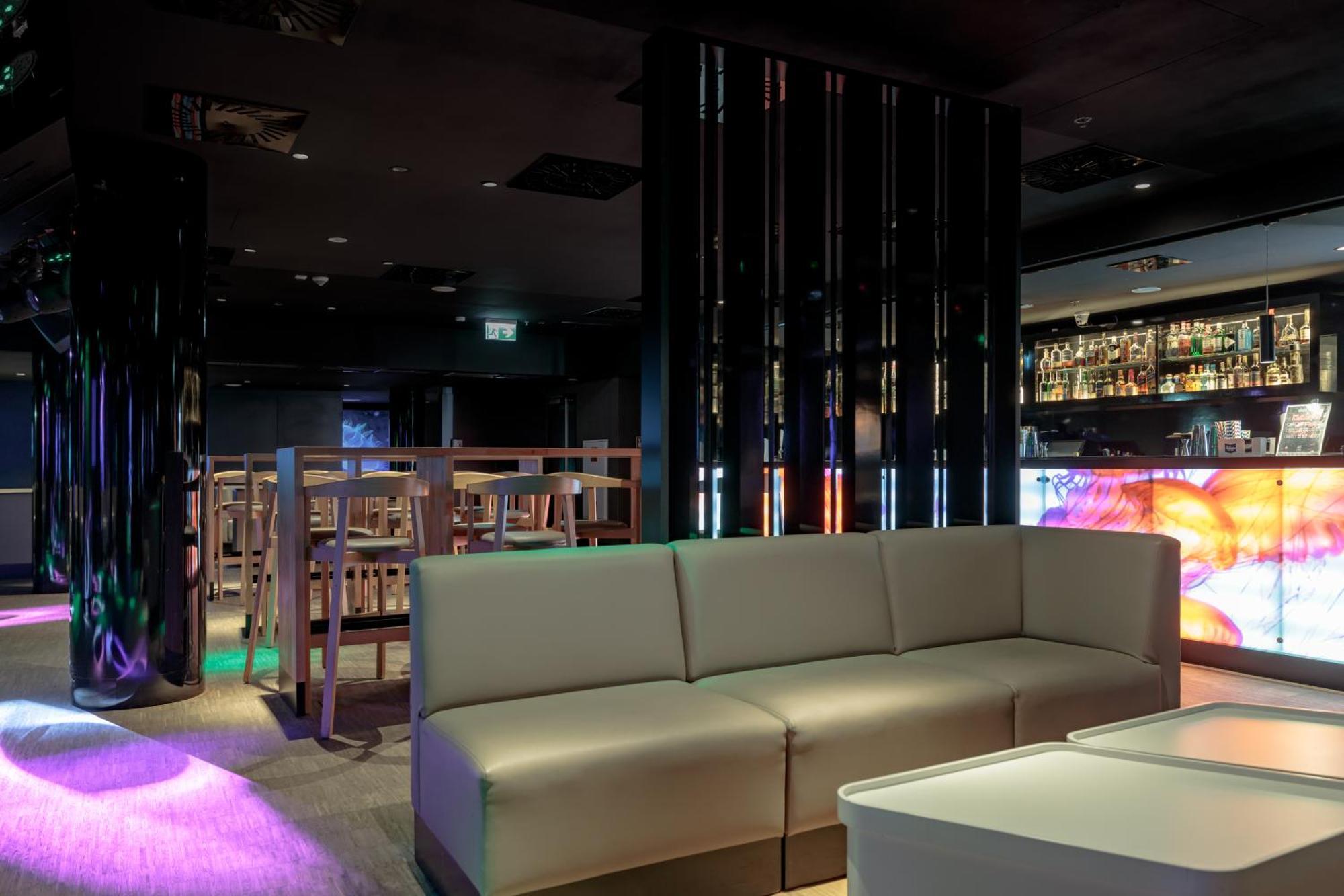 Radisson Blu Resort シフィノウイシチェ エクステリア 写真 The photo shows the interior of a stylish lounge or bar. The space features a modern design with dark walls and a sleek atmosphere. There is a beige sectional sofa in the foreground, providing a casual seating area. In the background, a bar is visibl