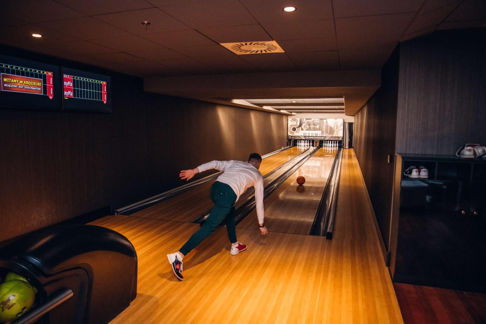 Radisson Blu Resort シフィノウイシチェ エクステリア 写真 The photo shows a bowling alley. In the foreground, a person is throwing a bowling ball down the lane. They are wearing a white top and green pants, with red and white shoes. The bowling lane is made of polished wood, and at the end of the lane, ther