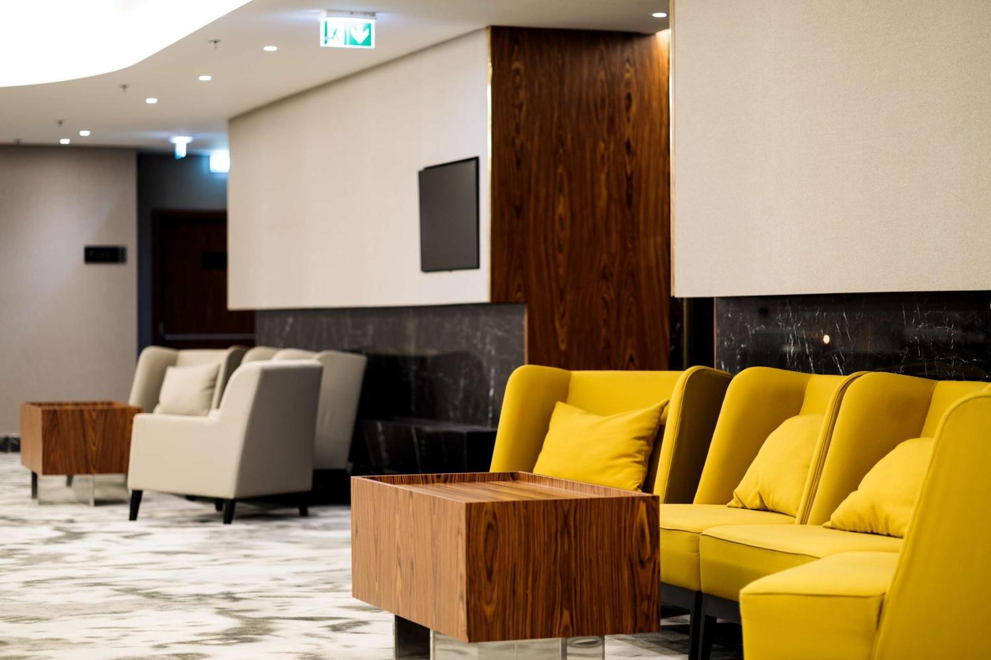 Radisson Blu Resort シフィノウイシチェ エクステリア 写真 The photo depicts a modern lounge or waiting area with stylish seating. On the left, there are soft gray armchairs arranged around a wooden coffee table. In the center, there are yellow chairs with plush cushions, contributing a vibrant contrast to t