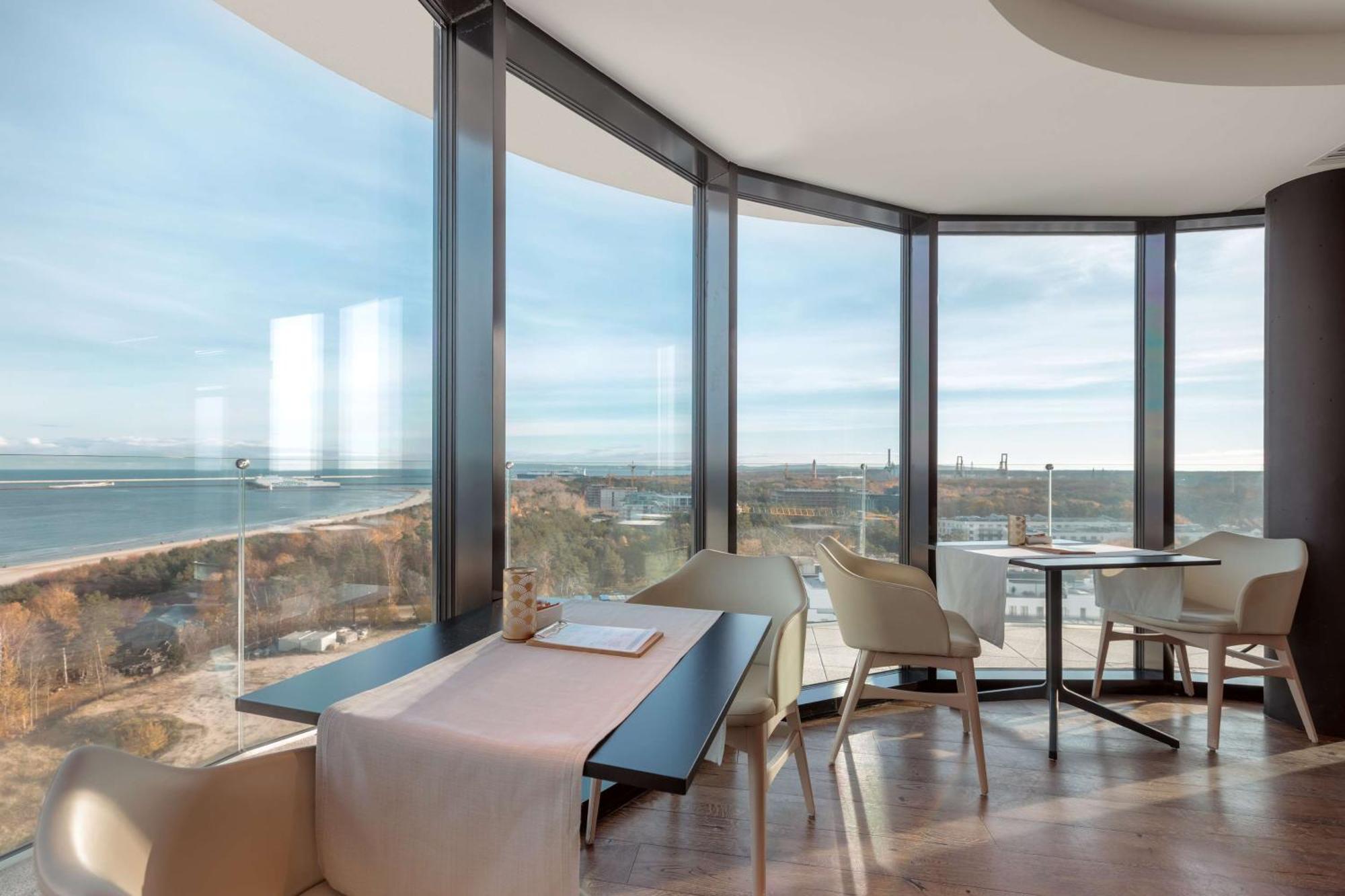 Radisson Blu Resort シフィノウイシチェ エクステリア 写真 The photo shows a modern dining area with large windows that offer a panoramic view of the landscape outside, including a body of water and possibly a shoreline. The design features sleek furniture, including a table with chairs arranged around it, a