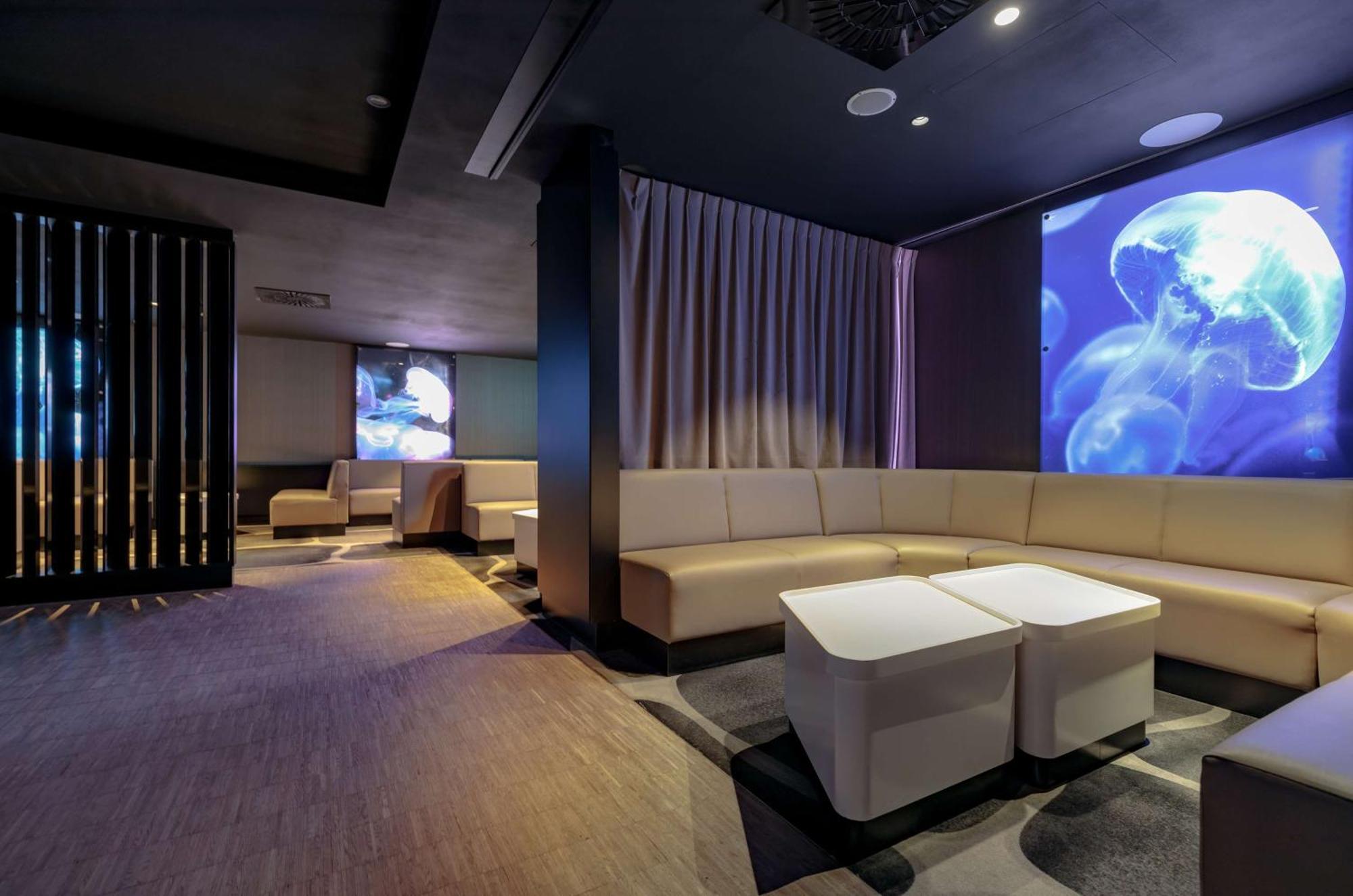Radisson Blu Resort シフィノウイシチェ エクステリア 写真 The photo shows a modern interior space that appears to be a lounge or relaxation area. The design is sleek and minimalist, featuring a curved, light-colored seating arrangement with low tables at the center. The walls are dark, contributing to a coz