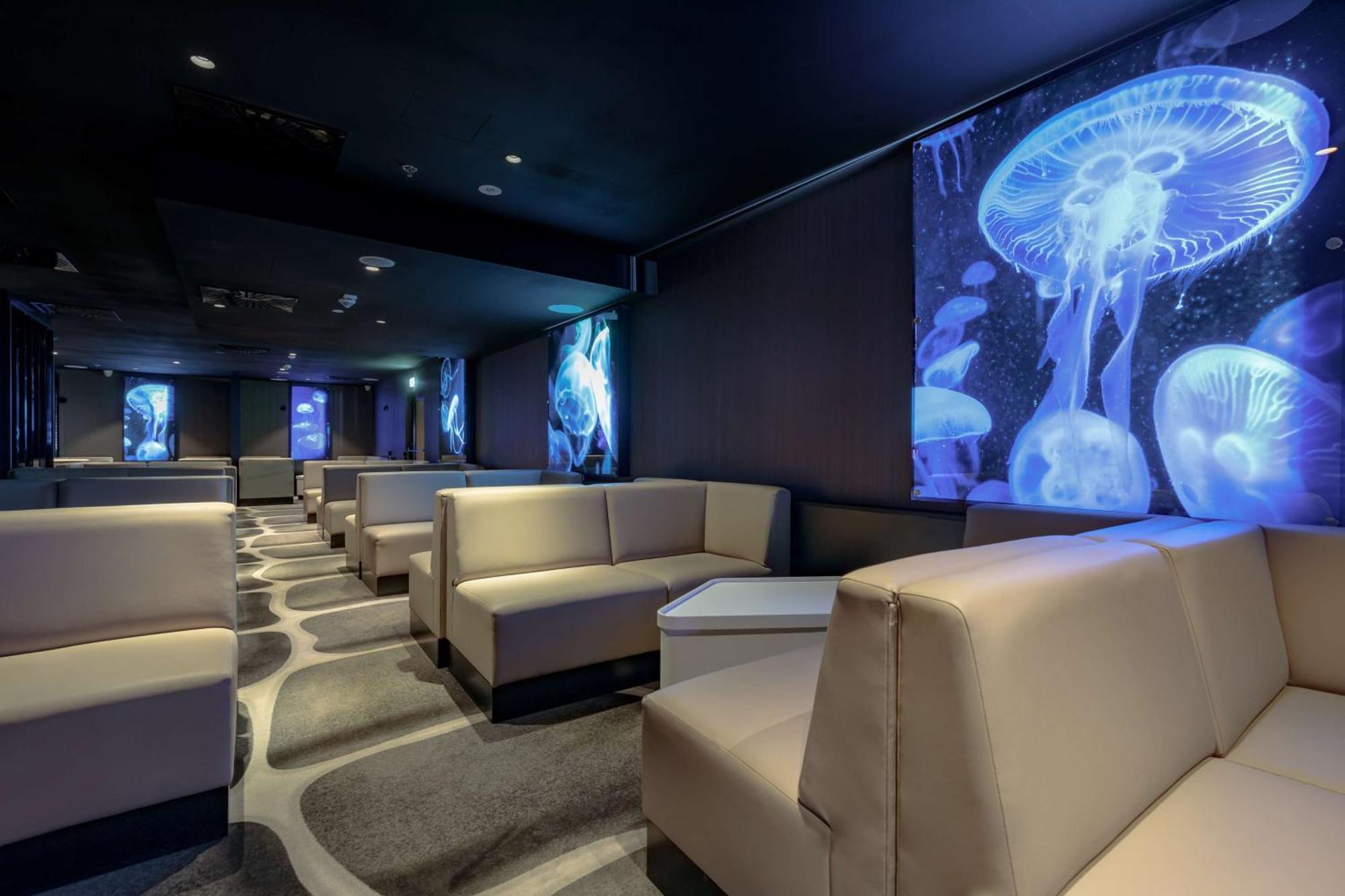 Radisson Blu Resort シフィノウイシチェ エクステリア 写真 The photo shows a modern lounge space with a sleek design. The area features light-colored, upholstered seating arranged in an open layout. The walls are decorated with large, vibrant images of jellyfish illuminated in blue, creating a calming underw