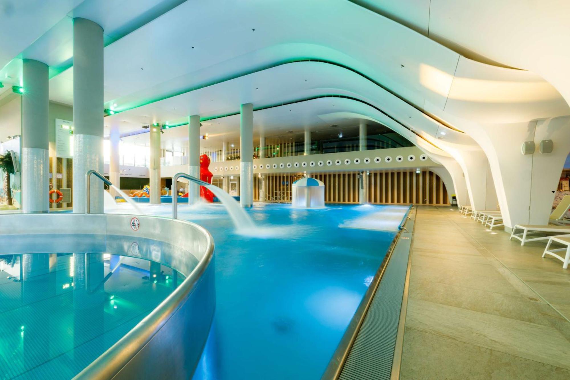 Radisson Blu Resort シフィノウイシチェ エクステリア 写真 The photo shows a modern indoor swimming pool area with an elegant design. The pool features curved edges and is filled with clear, blue water. There are various amenities, such as jets for relaxation and possibly seating areas along the edges. The l