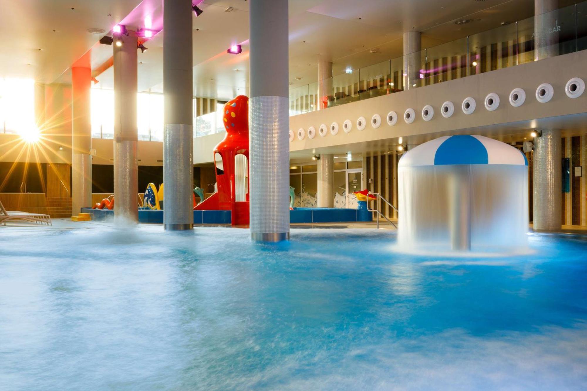 Radisson Blu Resort シフィノウイシチェ エクステリア 写真 The photo shows an indoor water park or pool area. There is a large body of water with playful features, including a water slide shaped like a red bear and a smaller structure with a blue and white canopy. The lighting is bright, suggesting a sunny a