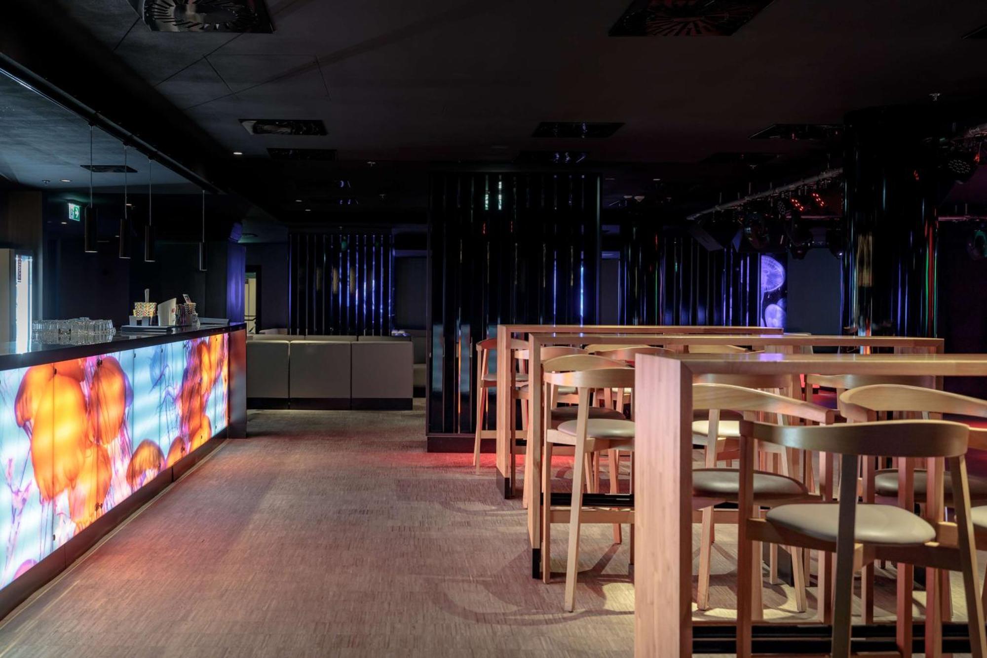 Radisson Blu Resort シフィノウイシチェ エクステリア 写真 The photo shows the interior of a modern bar or nightclub. It features a sleek and stylish design with a long bar counter illuminated by colorful lights. The floor has a neutral carpet, and there are wooden high-top tables with accompanying chairs ar