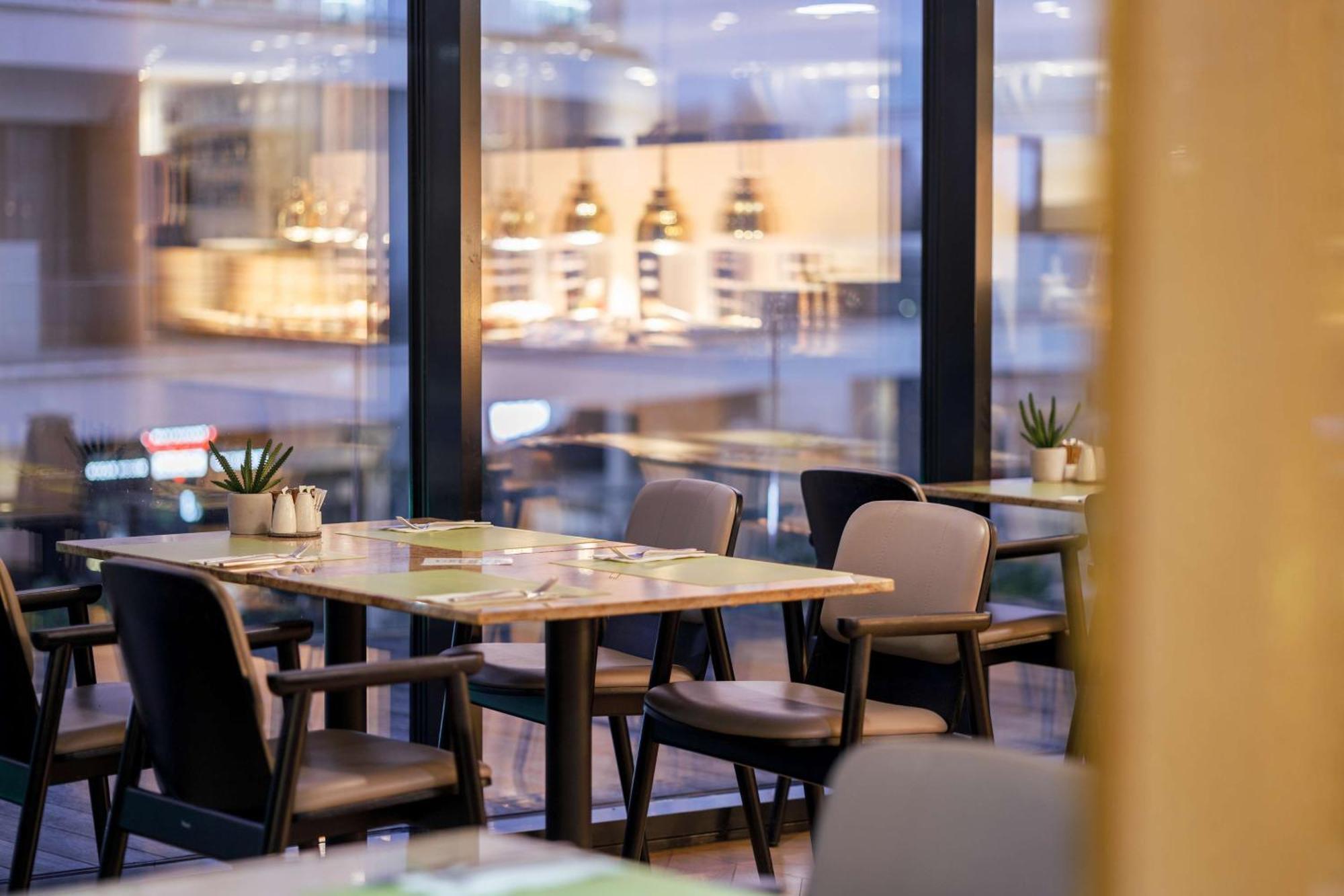 Radisson Blu Resort シフィノウイシチェ エクステリア 写真 The photo shows a modern restaurant interior featuring several tables and chairs arranged under large windows. The tables are set with green placemats and cutlery. There are small potted plants on the tables, adding a touch of decor. In the backgroun
