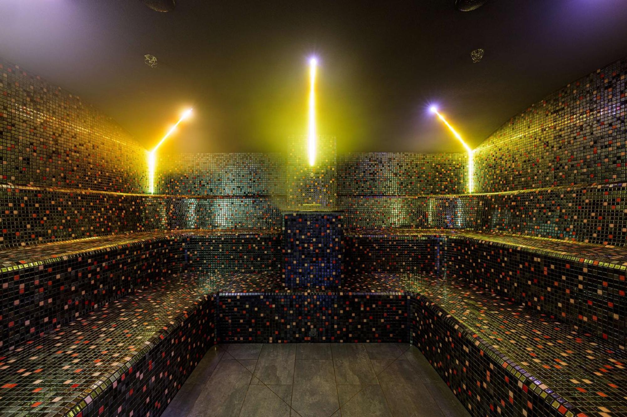 Radisson Blu Resort シフィノウイシチェ エクステリア 写真 The photo shows the interior of a steam room or sauna. The space is characterized by a series of benches that are built into the walls, allowing for multiple seating options. The walls are adorned with a mosaic of small, colorful tiles that create a 
