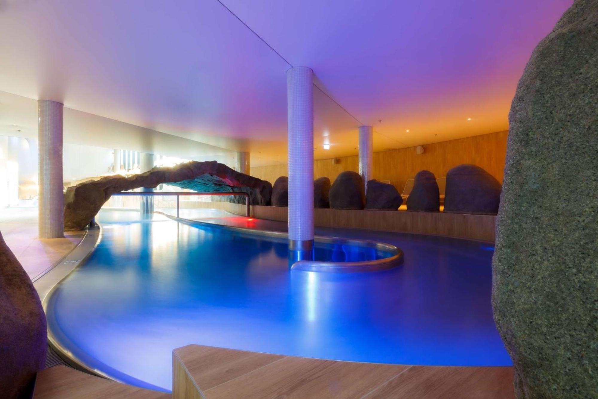 Radisson Blu Resort シフィノウイシチェ エクステリア 写真 The photo showcases an elegant indoor swimming pool area. The pool has a flowing, organic shape and is illuminated with soft blue and purple lighting, creating a calming ambiance. Surrounding the pool are smooth, natural-looking stones and wooden ele