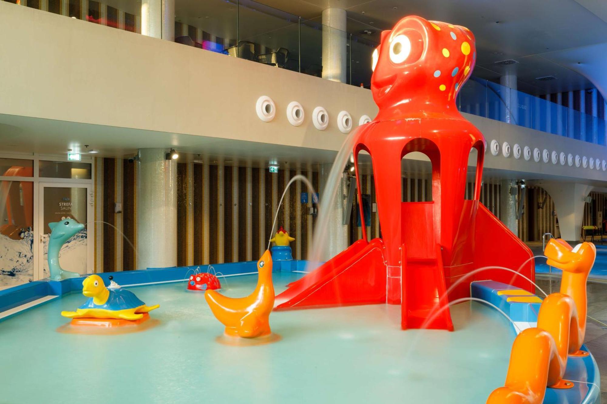 Radisson Blu Resort シフィノウイシチェ エクステリア 写真 The photo shows a colorful indoor splash pad or water play area designed for children. Central to the scene is a large, bright red octopus structure, which has water fountains spraying out. Surrounding it are various playful, colorful water animals, 