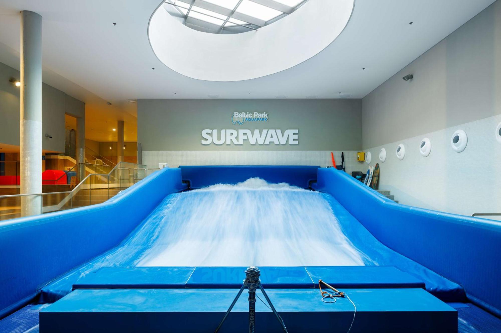Radisson Blu Resort シフィノウイシチェ エクステリア 写真 The photo shows an indoor surfing attraction called "Surfwave." It features a large blue ramp with water flowing down it, creating a wave-like effect for surfing. Above the ramp, there is a sign that says "SURFWAVE." The area appears well-lit and mod
